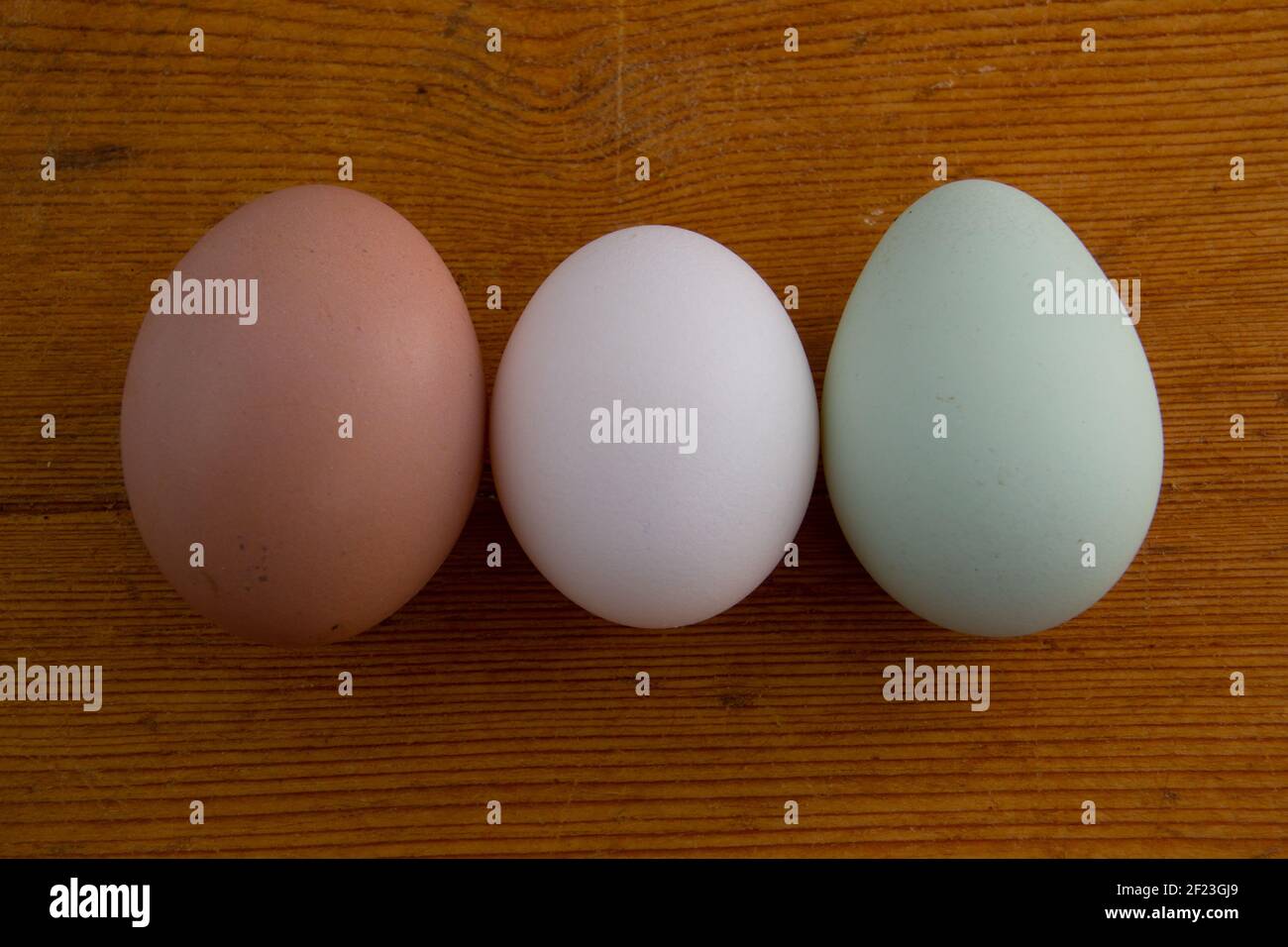 White, brown and green Araucana chicken egg laying on a wooden cutting board with copy space Stock Photo