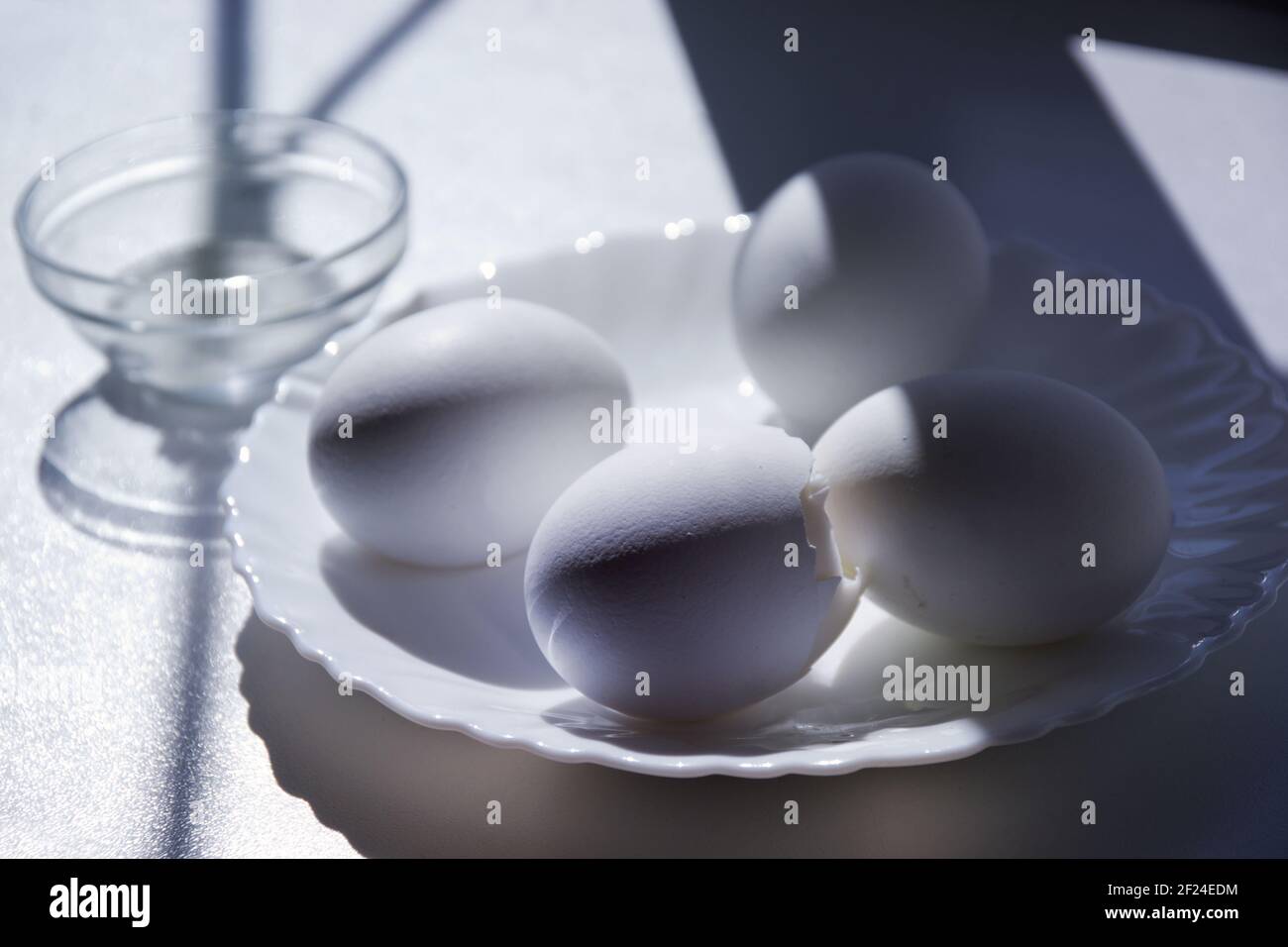 four boiled eggs on white windowsill in the sunlight in elegant little white porcelain plate. one slice open Stock Photo