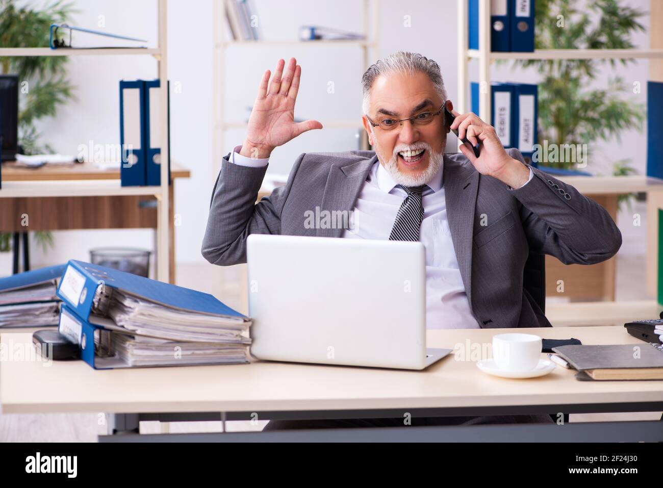 Old male employee using phone in the office Stock Photo