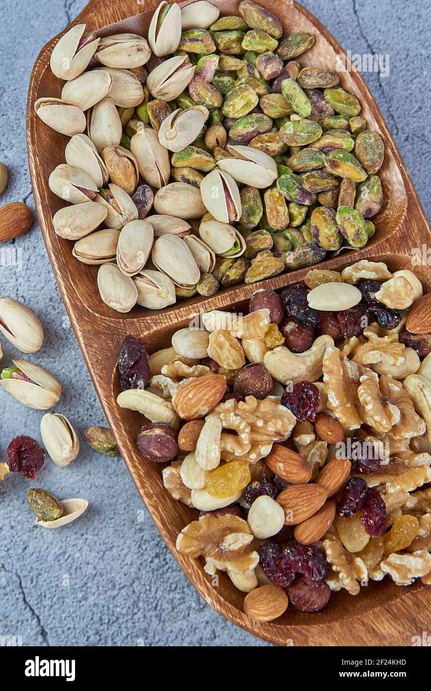 Mix dried fruits with nuts, pistachios, cashew nuts in wooden bowl on gray concrete background. Stock Photo