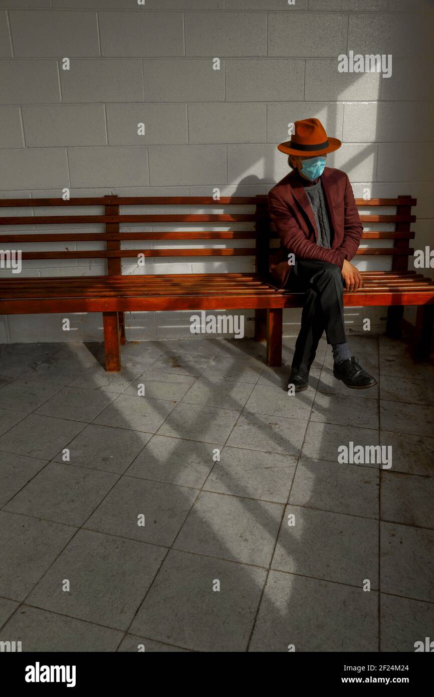 Man with hat wearing mask sitting on the bench Stock Photo