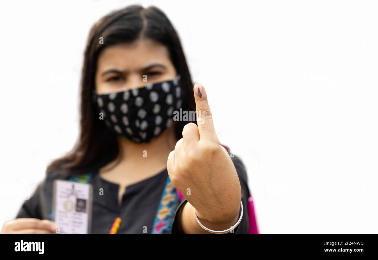 selective focus on ink-marked finger of an Indian woman with safety face mask and voter card on other hand Stock Photo