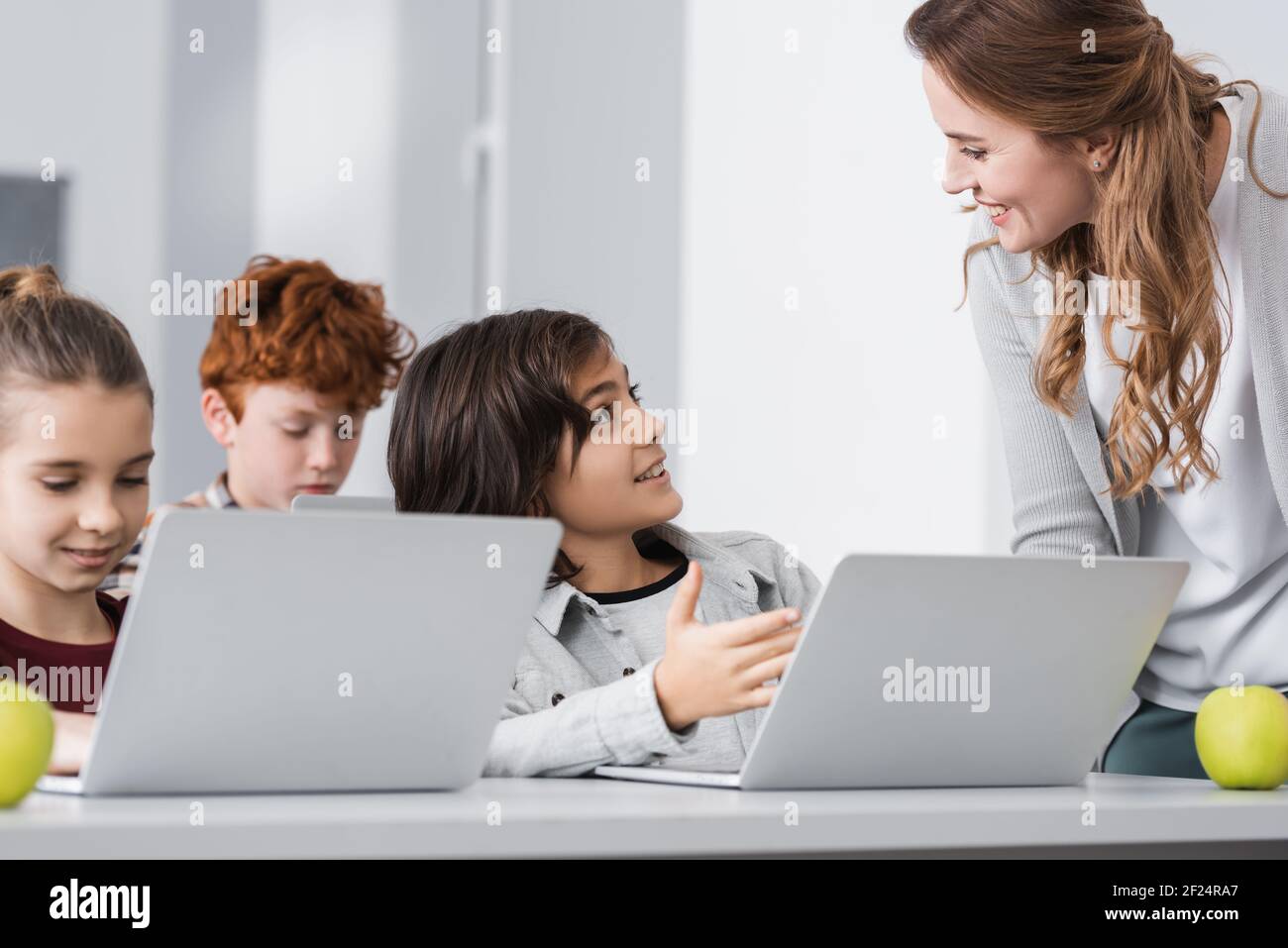 schoolboy pointing at laptop near smiling teacher in classroom Stock ...