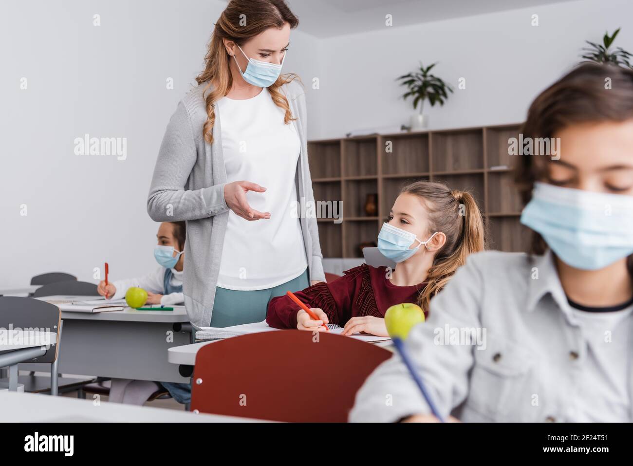 teacher in medical mask pointing with finger near girl during lesson Stock Photo