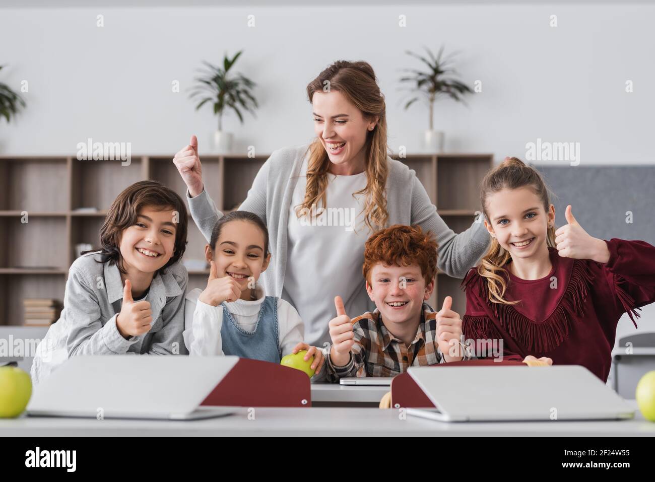 excited schoolkids and teacher showing thumbs up in classroom Stock Photo