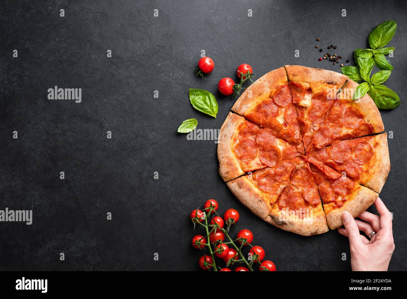 Hand taking slice of pepperoni pizza. Black stone concrete background, top view with copy space for text or design elements. Eating unhealthy fast foo Stock Photo