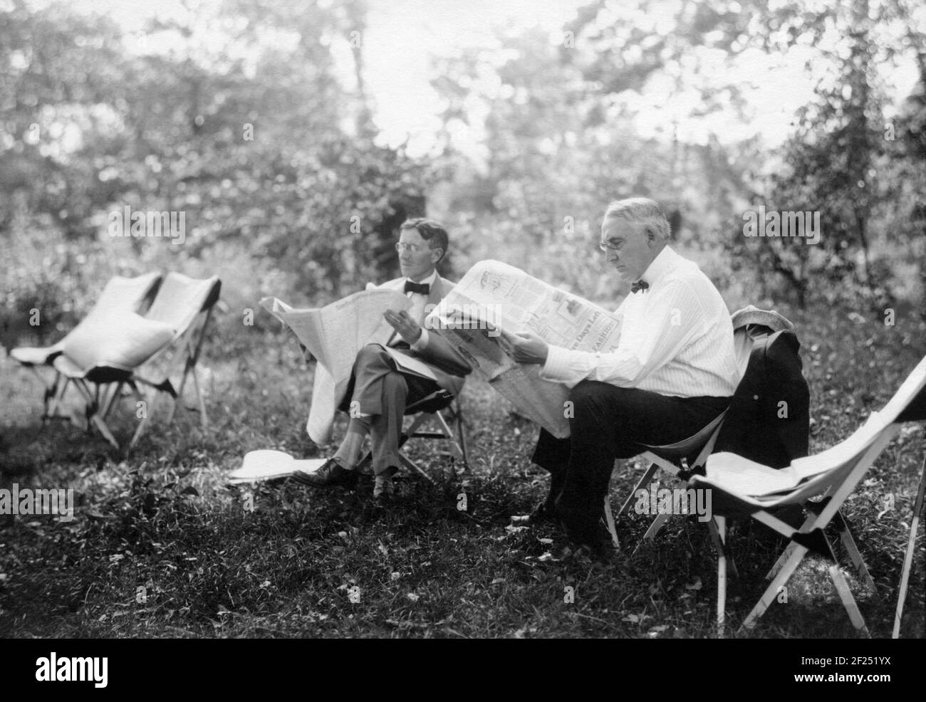 U.S. President Warren G. Harding and Harvey S. Firestone, founder of Firestone Tire & Rubber Company, reading newspapers on a camping trip in Maryland in 1921. Between 1914 and 1924 a group of prominent American leaders and innovators (who dubbed themselves "the vagabonds") took annual camping trips and adventures around the country. The group included Henry Ford, Thomas Edison, Harvey Firestone, and John Burroughs. In 1921 they were joined by President Warren Harding at a campsite that became known as "Camp Harding" and Secret Service patrolled the woods surrounding the camp. Stock Photo