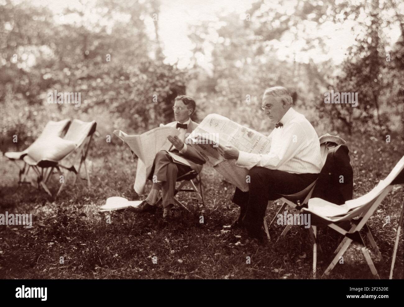 U.S. President Warren G. Harding and Harvey S. Firestone, founder of Firestone Tire & Rubber Company, reading newspapers on a camping trip in Maryland in 1921. Between 1914 and 1924 a group of prominent American leaders and innovators (who dubbed themselves 'the vagabonds') took annual camping trips and adventures around the country. The group included Henry Ford, Thomas Edison, Harvey Firestone, and John Burroughs. In 1921 they were joined by President Warren Harding at a campsite that became known as 'Camp Harding' and Secret Service patrolled the woods surrounding the camp. Stock Photo