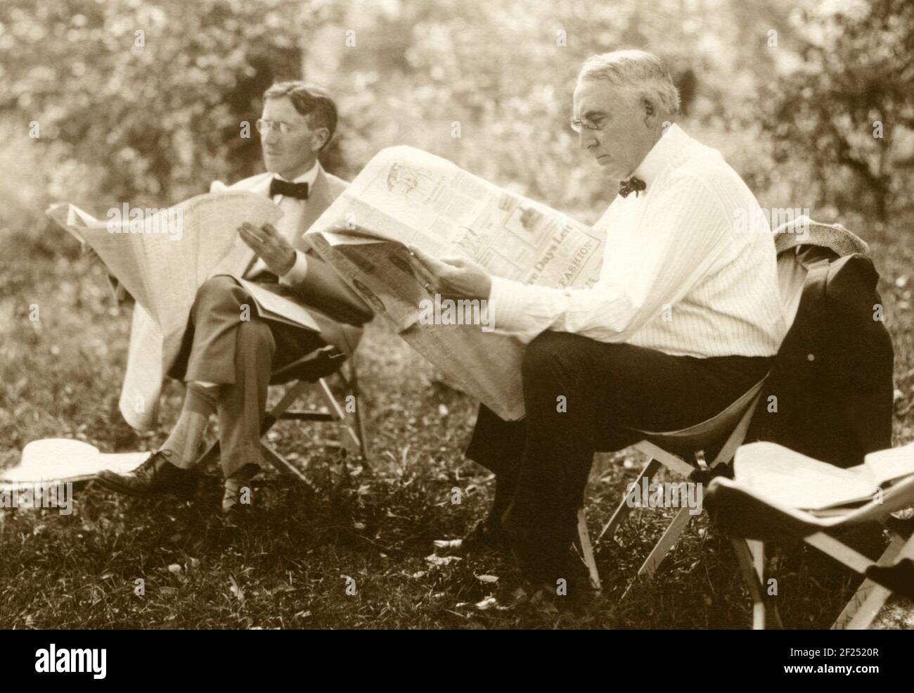 U.S. President Warren G. Harding and Harvey S. Firestone, founder of Firestone Tire & Rubber Company, reading newspapers on a camping trip in Maryland in 1921. Between 1914 and 1924 a group of prominent American leaders and innovators (who dubbed themselves 'the vagabonds') took annual camping trips and adventures around the country. The group included Henry Ford, Thomas Edison, Harvey Firestone, and John Burroughs. In 1921 they were joined by President Warren Harding at a campsite that became known as 'Camp Harding' and Secret Service patrolled the woods surrounding the camp. Stock Photo