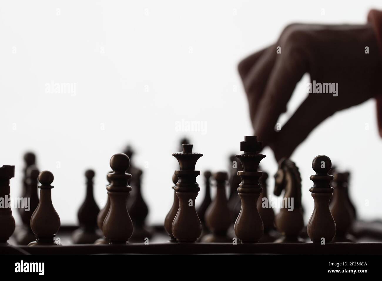 Dark silhouettes of Hand of player moving chess figure on chess board. Concept of strategy and tactic Stock Photo