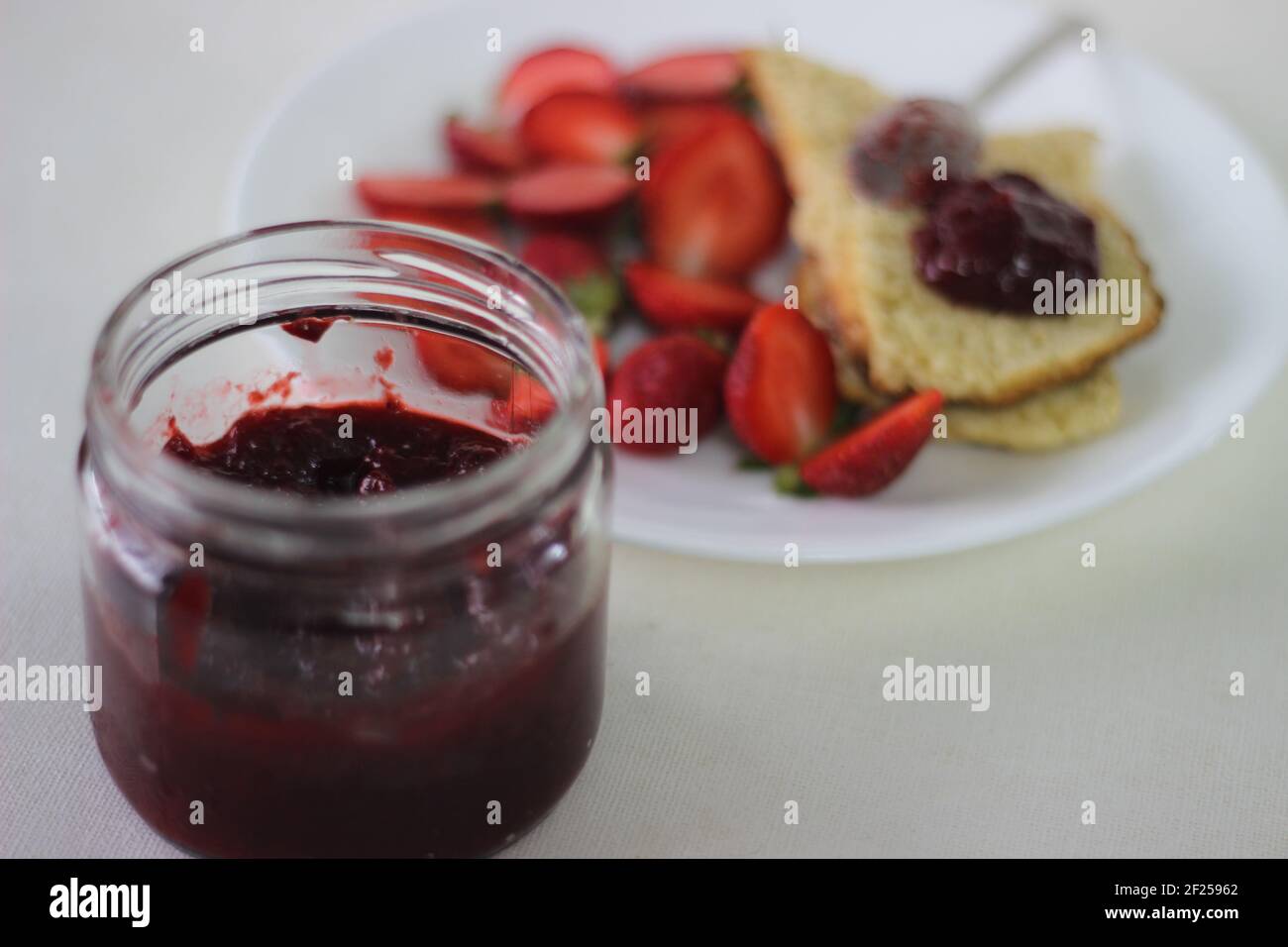 Half-full bottle with homemade strawberry jam shot along with home-baked plain mildly sweet buttermilk scones. Shot on white background Stock Photo