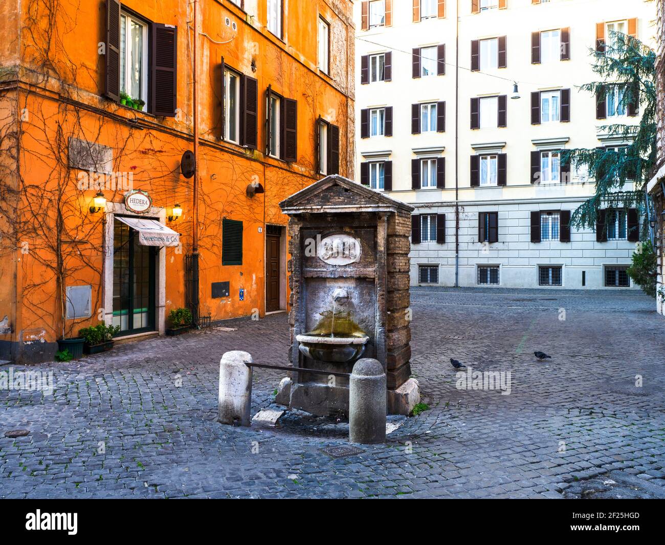 The fountain  in rione Borgo is protected by two small columns connected by an iron bar, consists of a simple rectangular travertine aedicule, gable at the top and leaning against a brick construction. The upper arch has a papal coat of arms - Rome, Italy Stock Photo