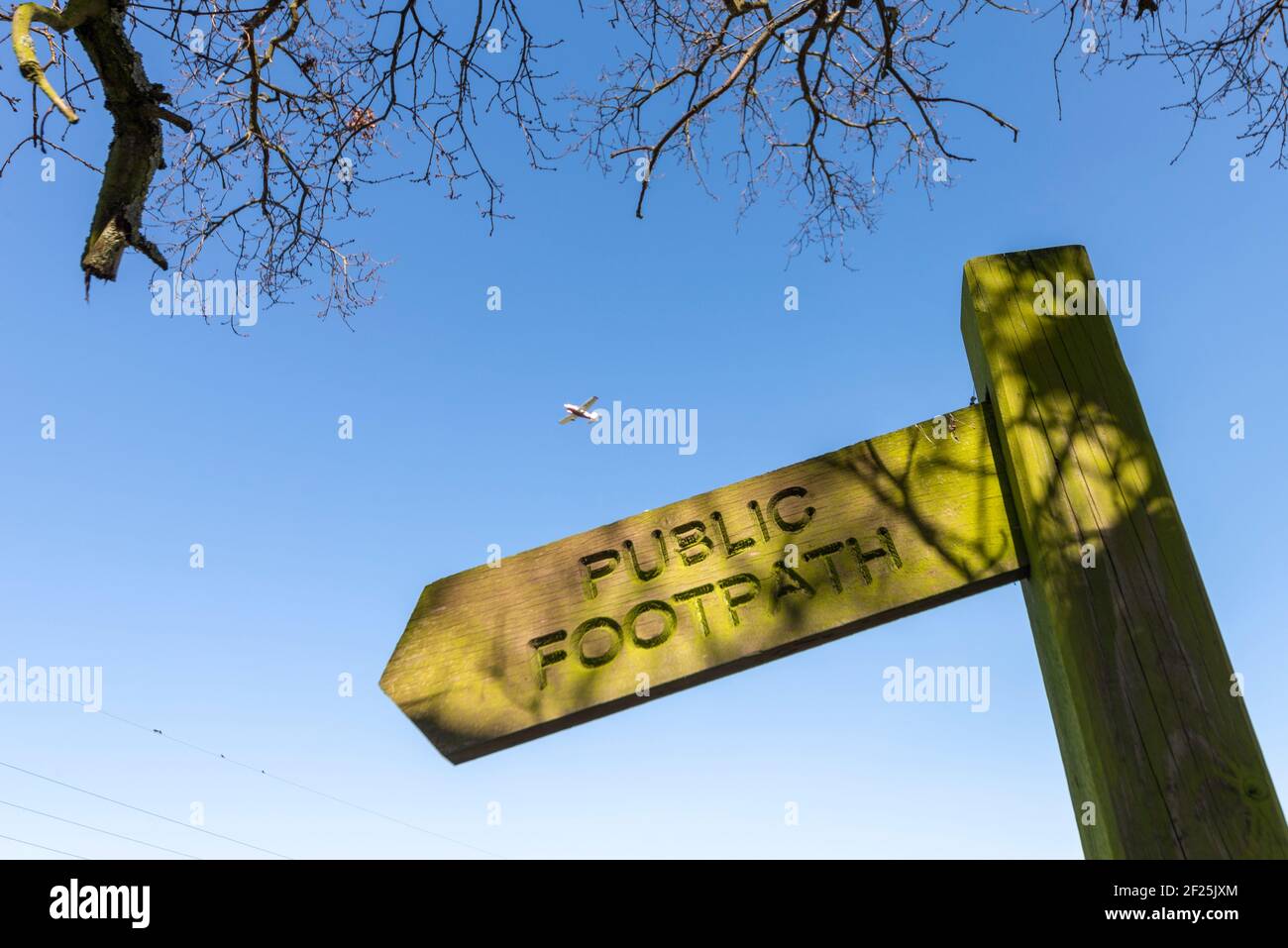 Old wooden public footpath sign in Rochford, Essex, UK, with a light aircraft plane on approach to land at London Southend Airport. Countryside travel Stock Photo