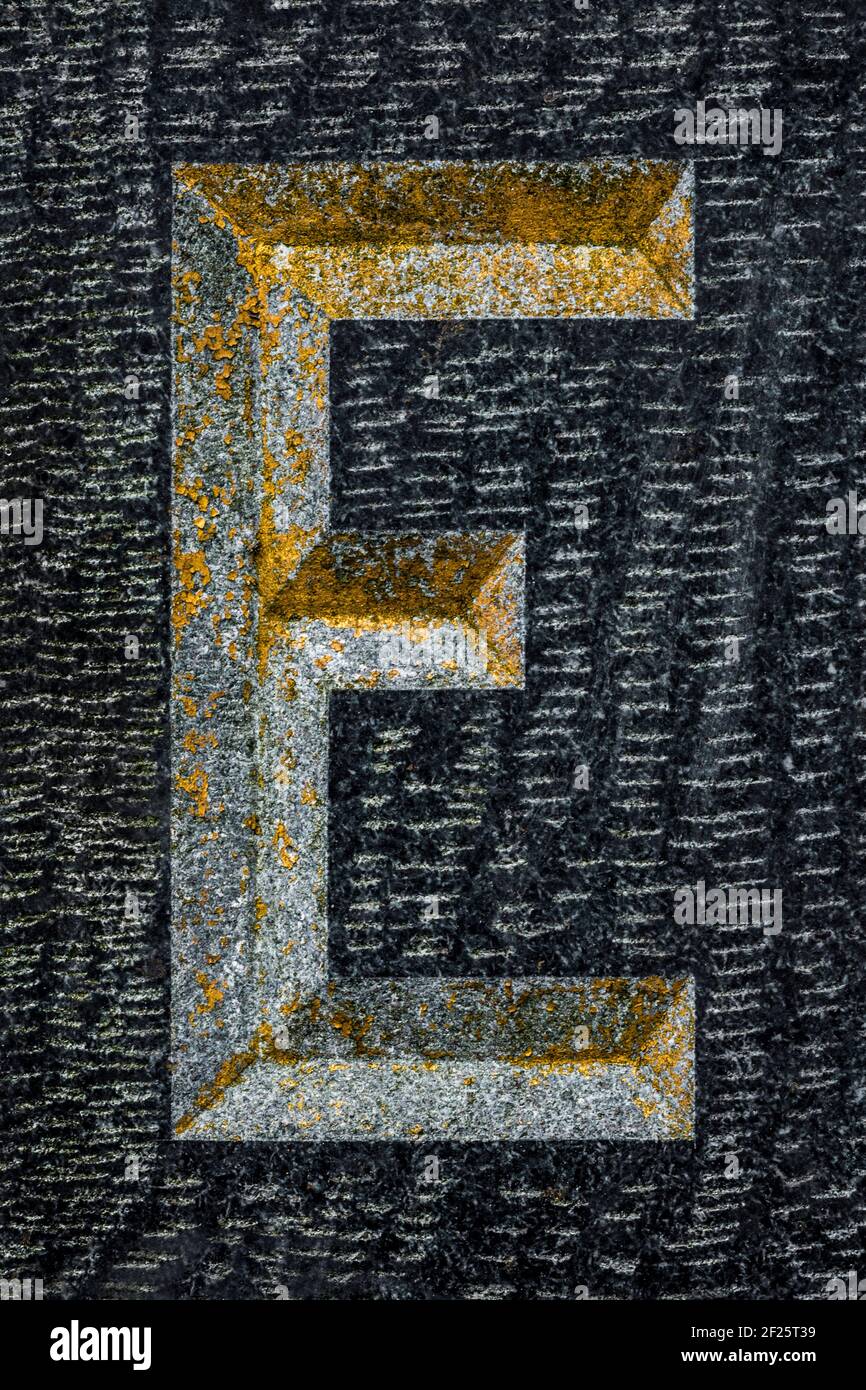 Golden weathered letter E on black granite Stock Photo