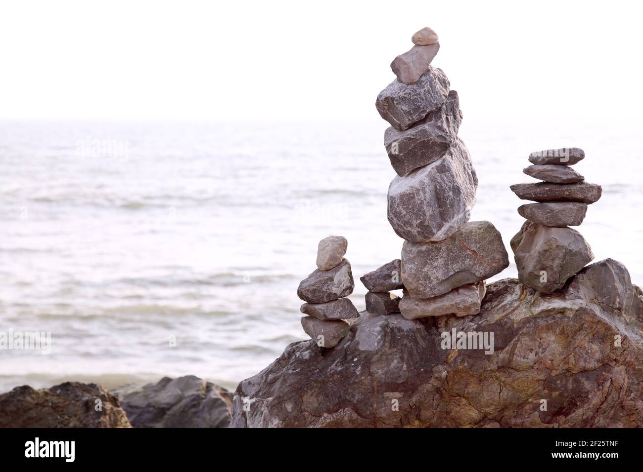 Art, discipline or hobby of balancing stones or stacking rocks to make rock or stone cairns. Balanced / stacked on beach shoreline with sea behind. Stock Photo