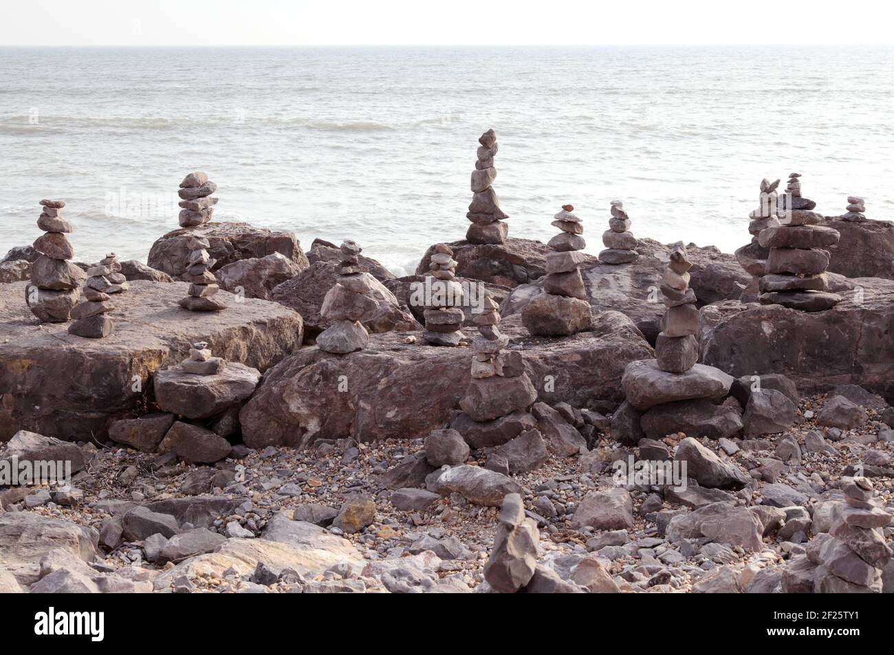 Stacks of balancing stones or balanced rocks to make rock or stone cairns. Stacked or piled on beach shoreline with sea behind. Stock Photo