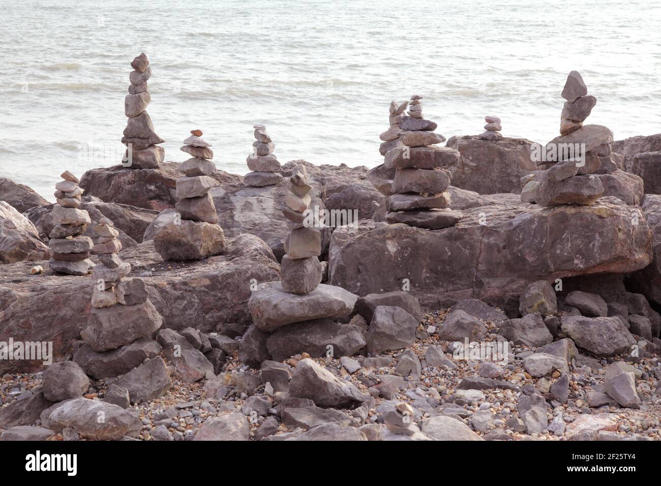 Stacks of balancing stones or balanced rocks to make rock or stone cairns. Stacked or piled on beach shoreline with sea behind. Stock Photo