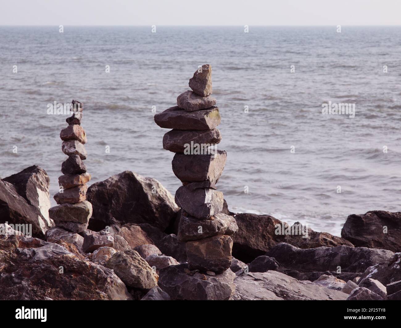 Balanced stones or balancing rocks. Piled or stacked to make rock or stone cairns on beach shoreline with sea behind. Stock Photo