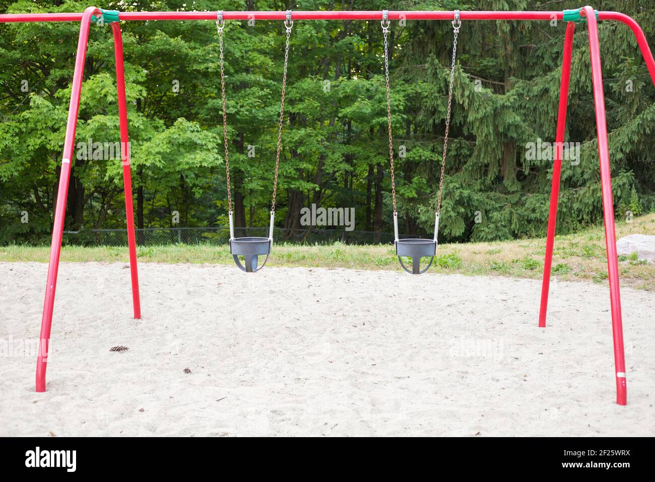 Swings for small children in the public park playground. Stock Photo