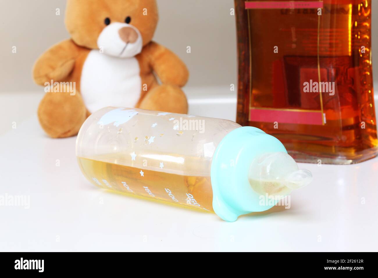 Symbol image of alcohol addiction in parents: cuddly toy, baby bottle and alcohol Stock Photo