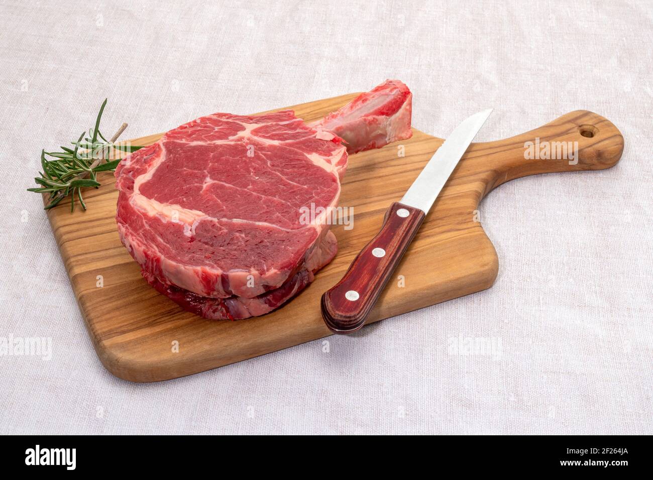 A raw rib eye tomahawk steak on a wooden cutting board Stock Photo