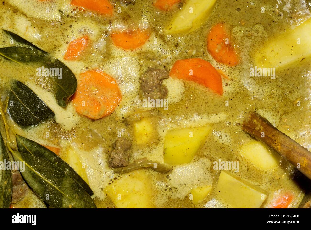 Beef stew simmering in a pot on a stove seen from directly above. Bay leaves visible with mixed vegetables and wooden spoon with copy space. Stock Photo