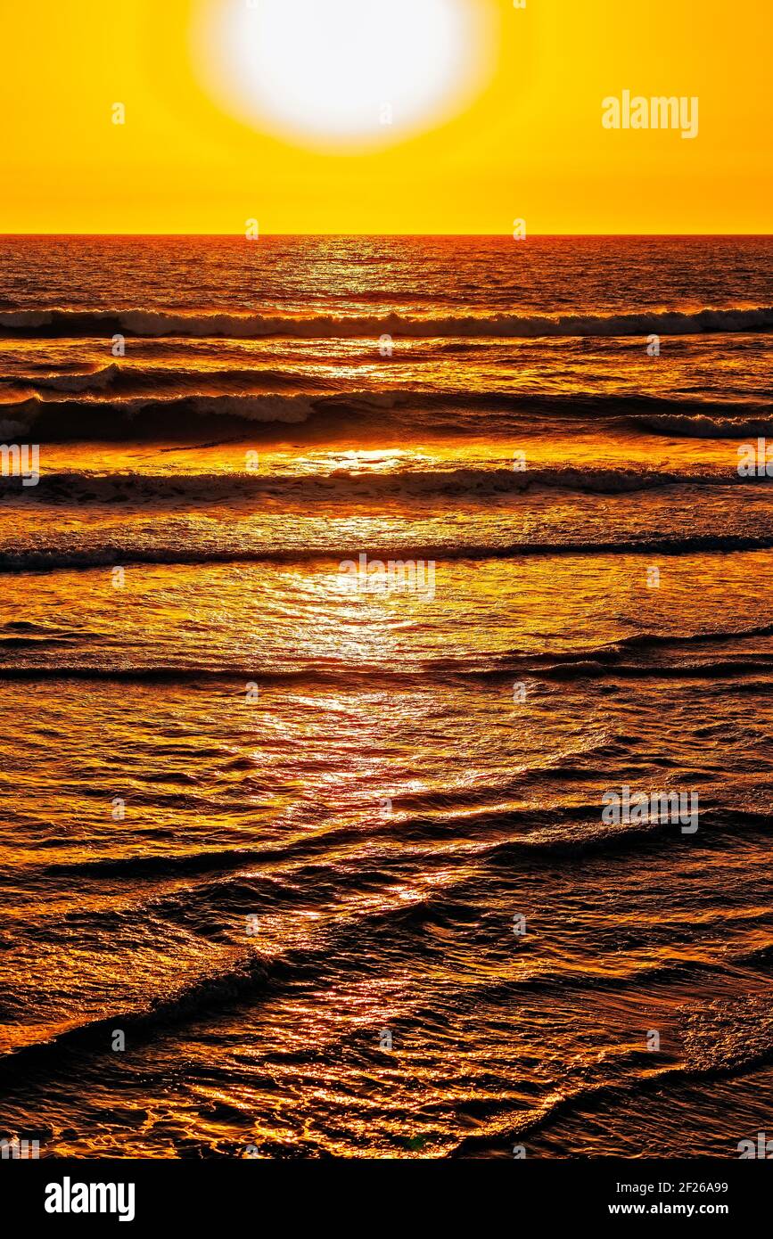 White globe in orange skies setting into amber seas. Stock Photo