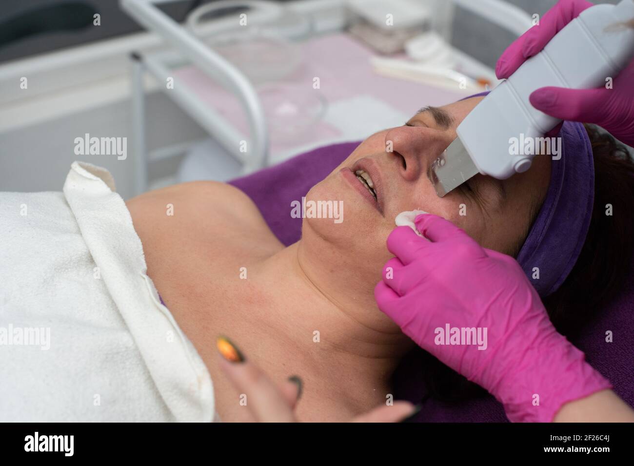 Cavitation device. The beautician gently guides the ultrasound device over the client's face to exfoliate the epidermis. Stock Photo