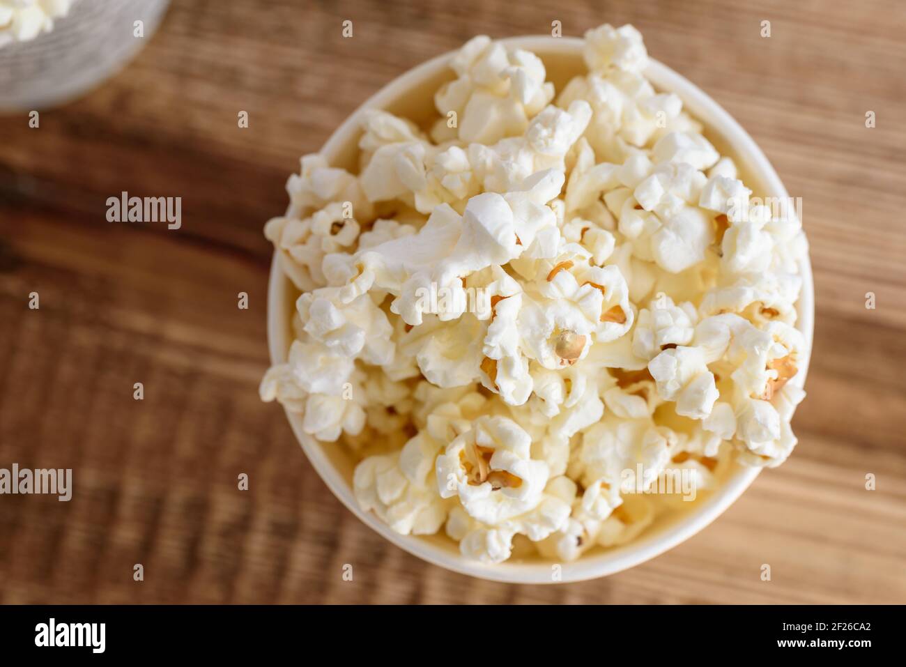 A bucket of popcorn, top-view, warm colors, light brown wooden background, flat lay, daylight macro close-up Stock Photo