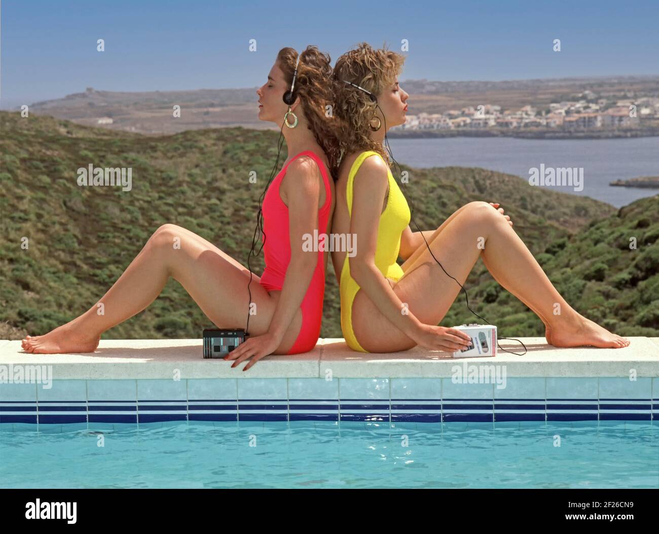 Historical 1980s archival view of two teenage girl friends on 80s Spanish  family villa package sunshine holiday where they had this idea to try out a  trendy girls back to back swimsuit