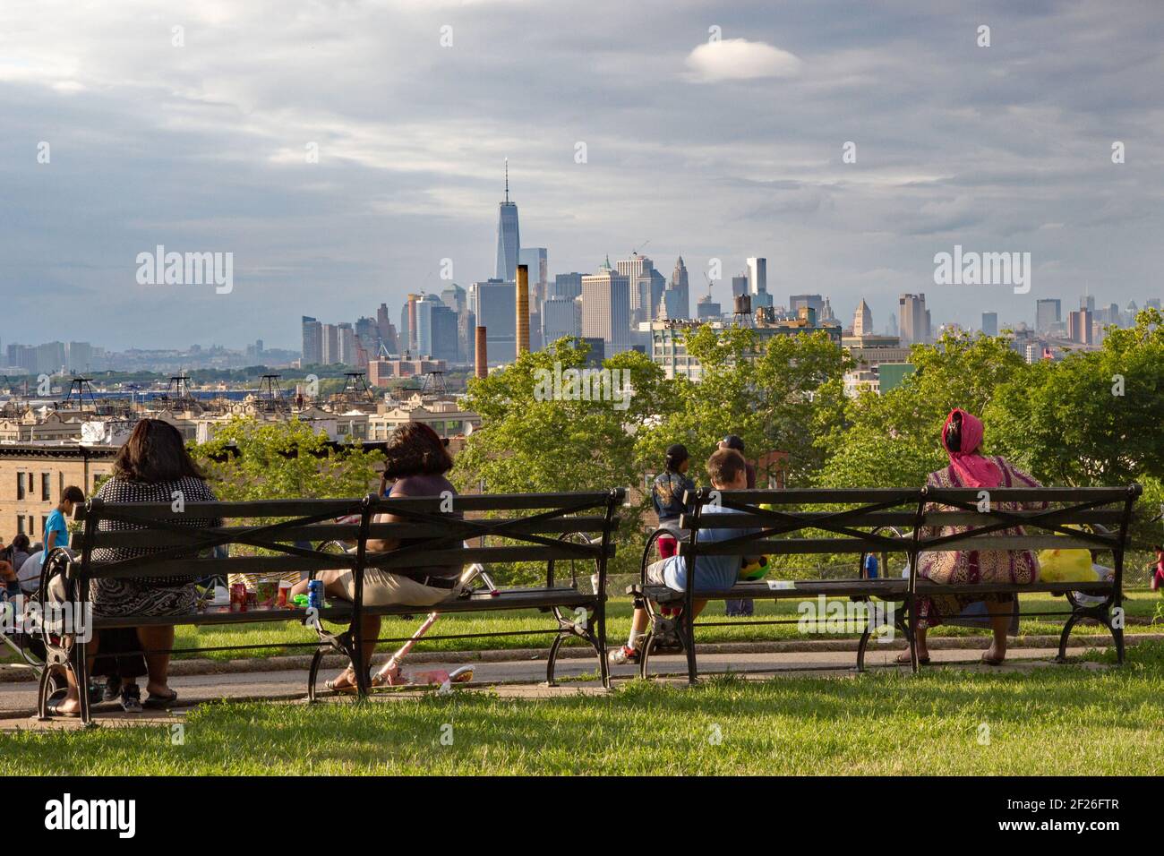 New York's diversity represented by people sat on a bench in Sunset Park, Brooklyn, admiring the view of Lower Manhattan on a sunny summer's day Stock Photo