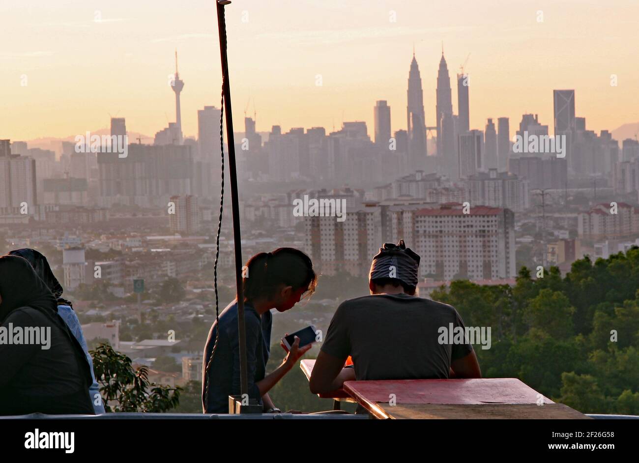 Iconic skyline of Kuala Lumpur at sunset with a young couples distracted by their smart phones Stock Photo