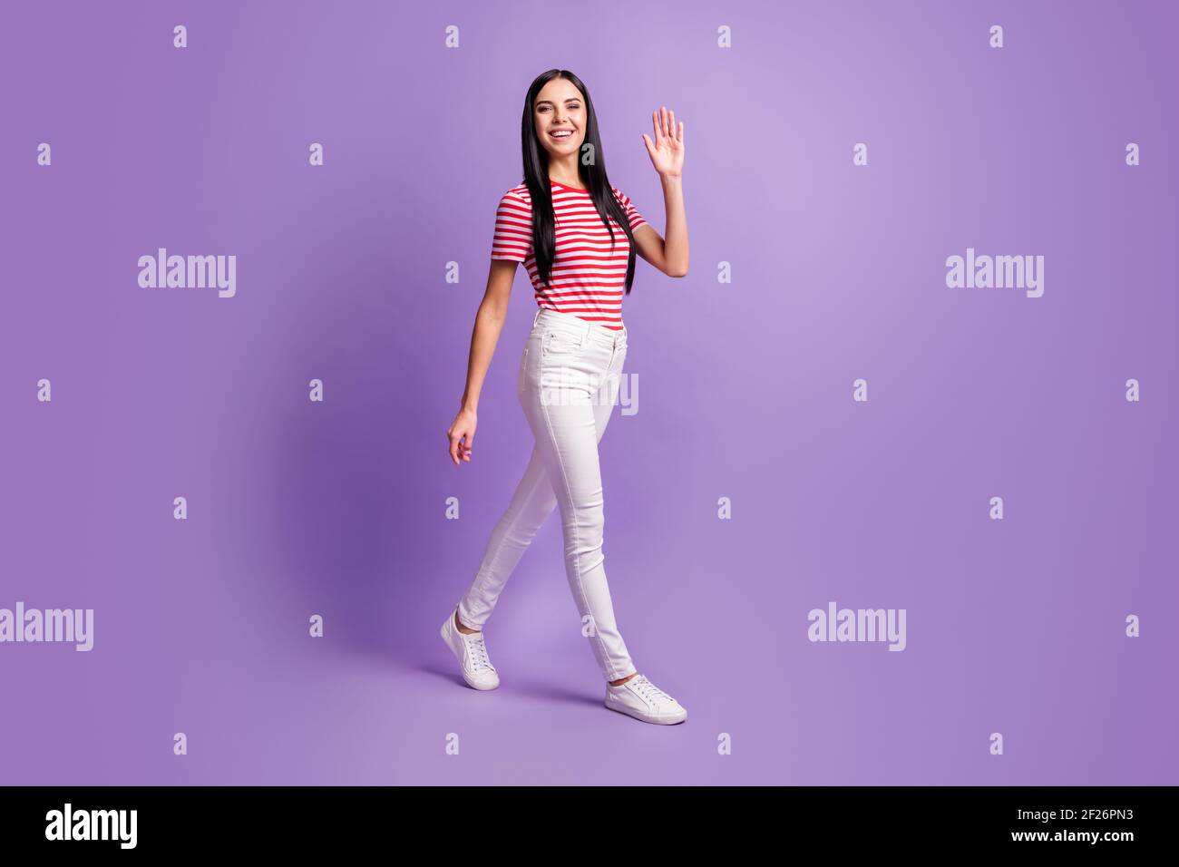 Full body profile side photo of cheerful pretty young lady walk by wave  hello isolated on purple color background Stock Photo - Alamy