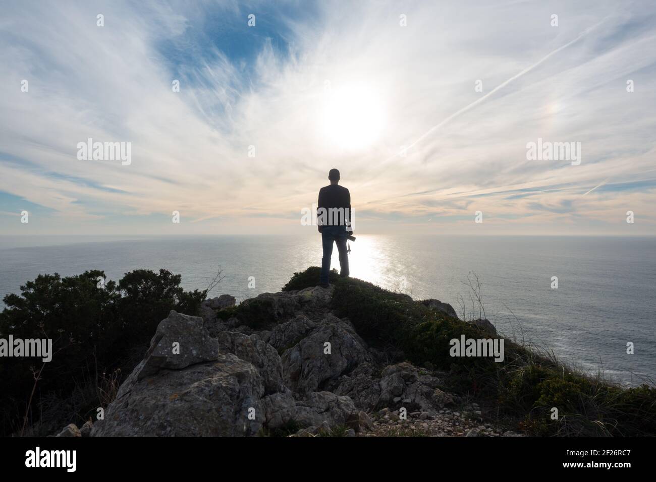 Man photographer silhouette with a camera on the hand on a cliff with the ocean sea on the background Stock Photo
