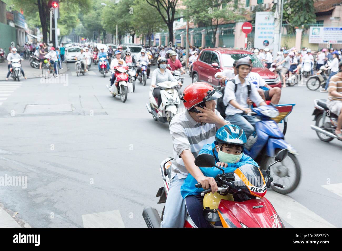 Vietnam, Ho Chi Minh City - Father and son on a scooter filled with other scooters during the early evening commute. Stock Photo