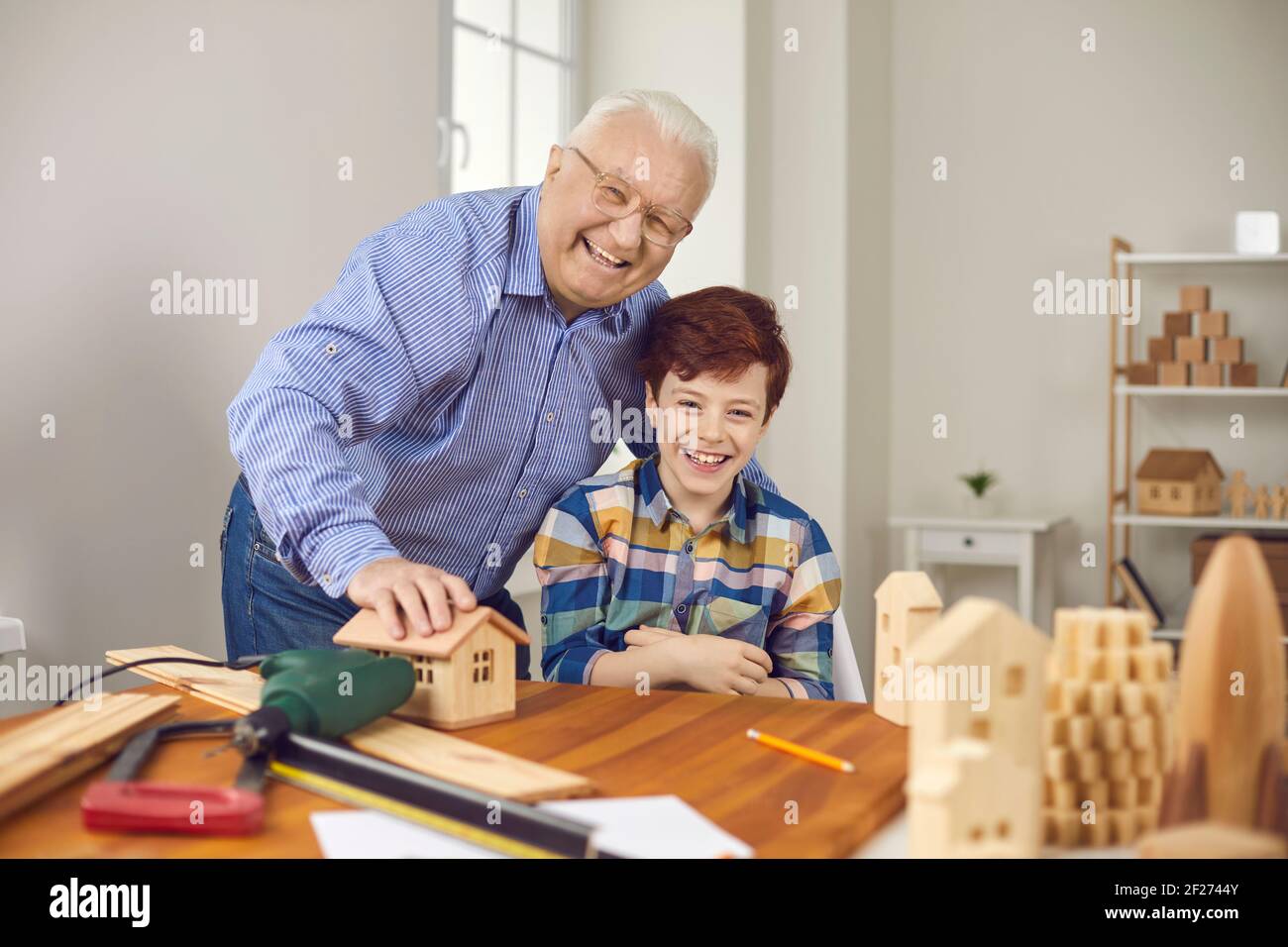 Happy grandpa and grandson making wooden toys and having fun in carpentry workshop Stock Photo