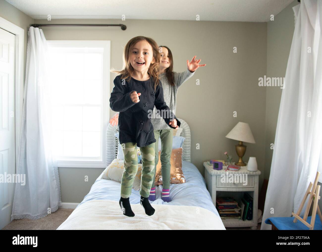 Two little girls jumping on the bed in sunny bedroom Stock Photo Alamy