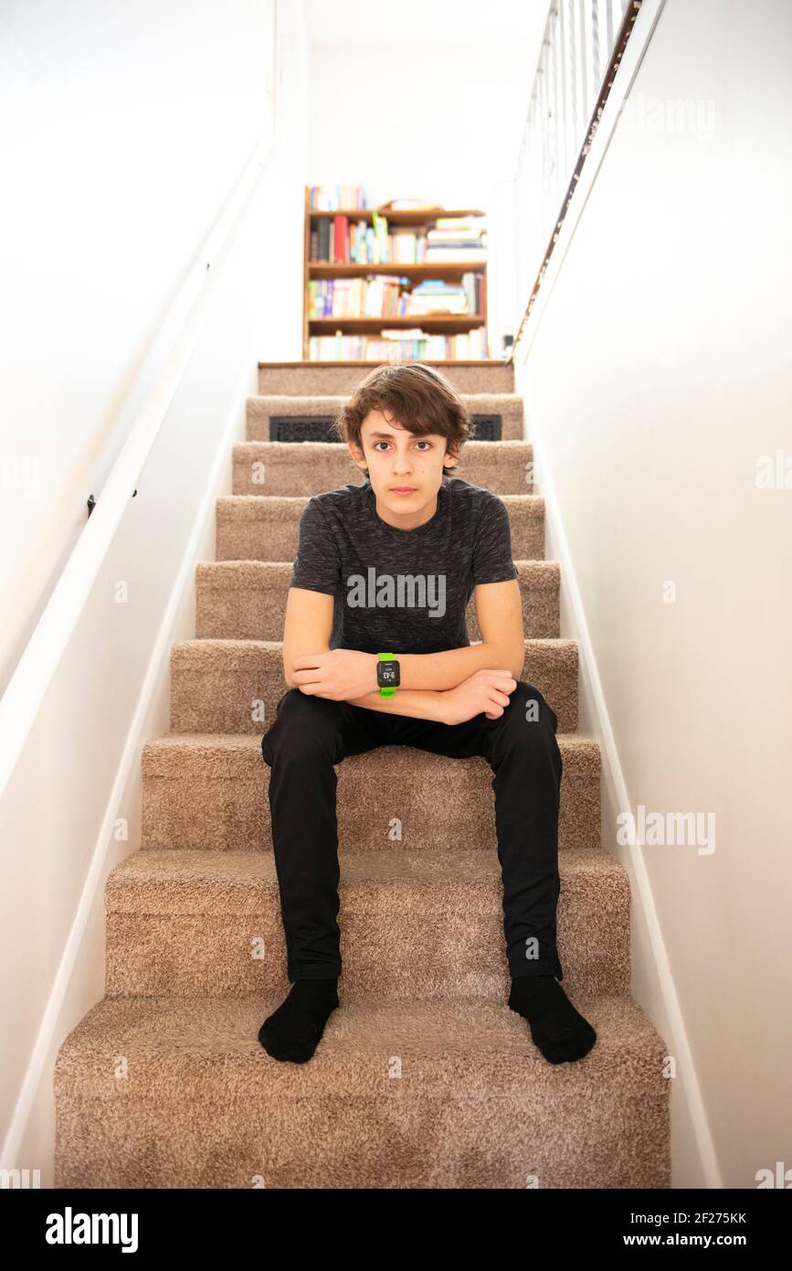 Handsome tween boy sitting on the steps in his house. Stock Photo