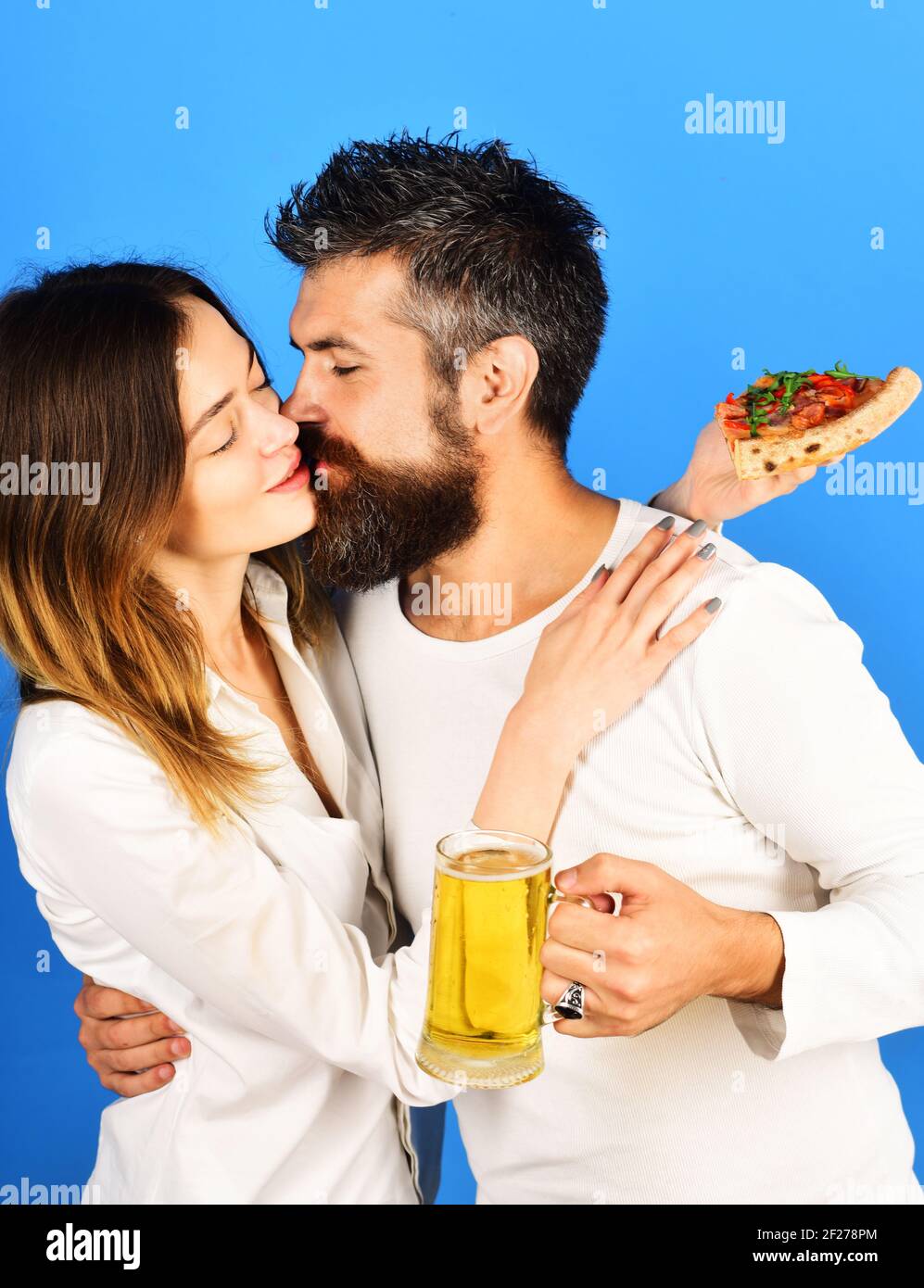 Beautiful couple drinking beer and eating pizza. Happy family time. Husband and wife eating pizza. Loving couple kissing. Stock Photo