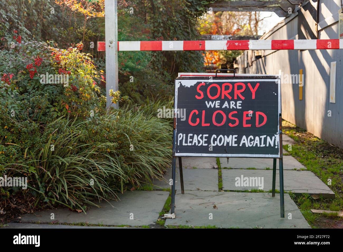 A large blackboard sign post in front of a shop says: ' Sorry We are closed, please come again.' There is a road block ahead. A concept image for buss Stock Photo