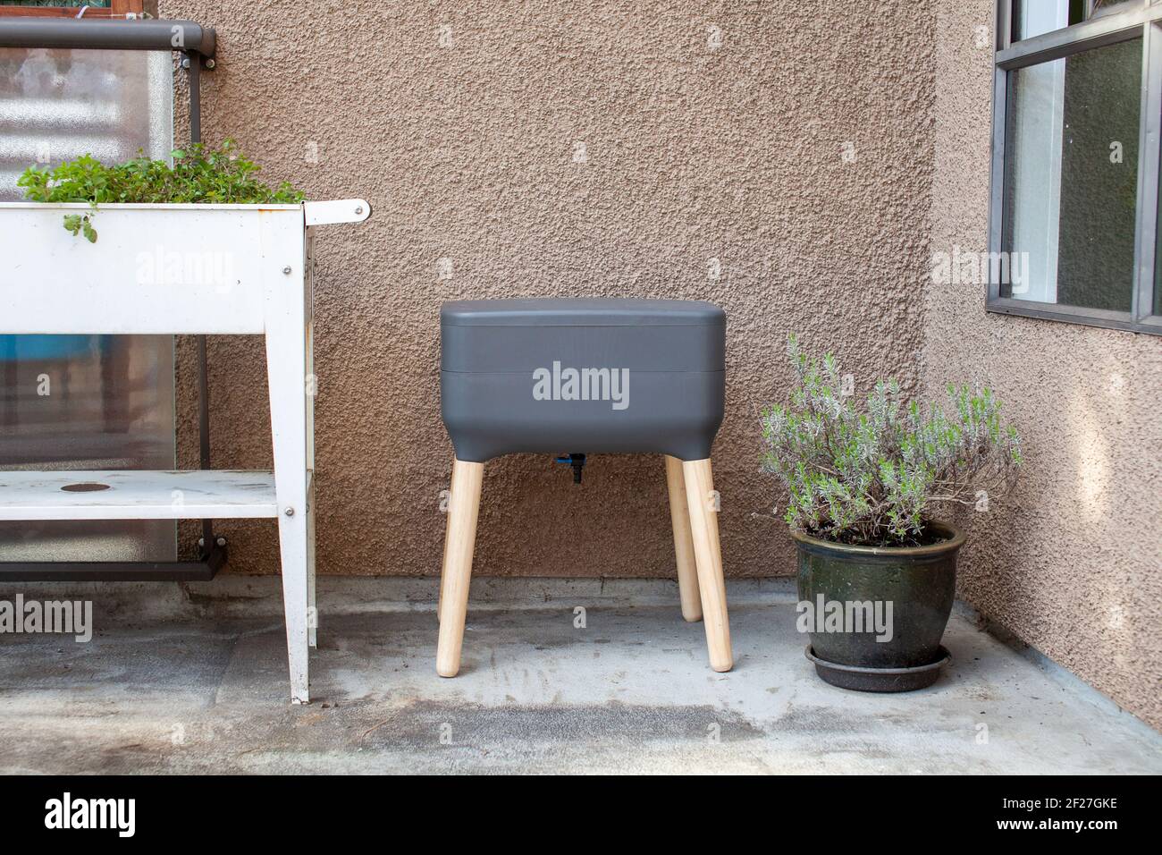 A vermicomposting system (worm composter) sits on an apartment balcony with other patio planters. Worms eat food scraps and produce worm castings and Stock Photo
