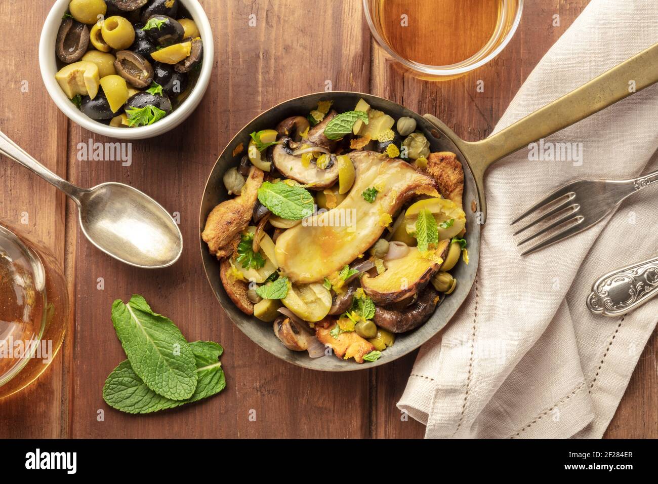 A rustic mushrooms and olives saute, shot from the top in a cast iron pan with mint and wine Stock Photo