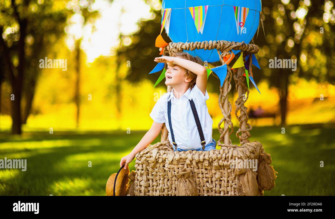 Little boy in a basket of a balloon with a straw hat in his hands looks into the distance in front of him. Stock Photo