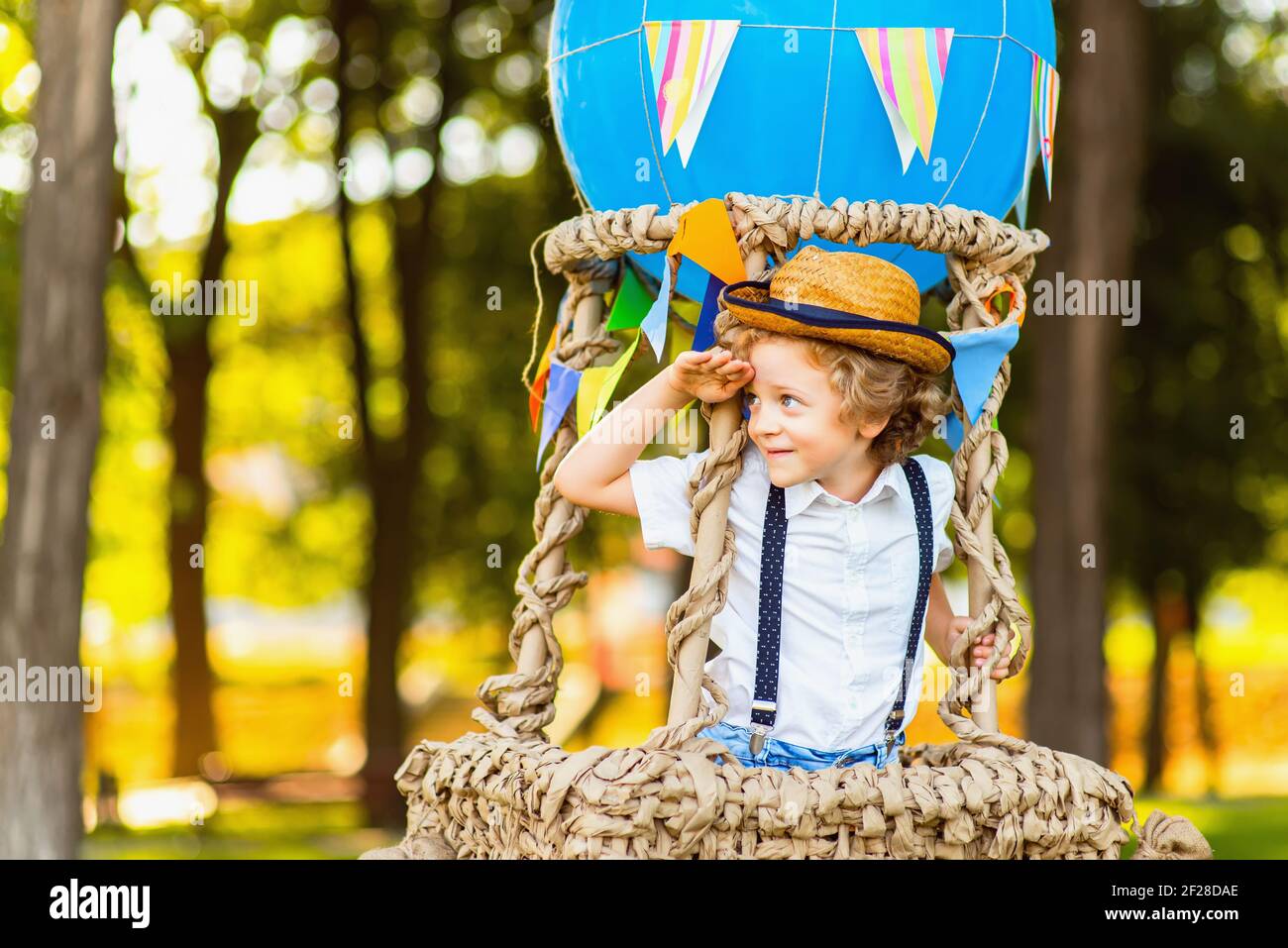 Little curly boy in a basket of a toy balloon looks into the distance. Stock Photo