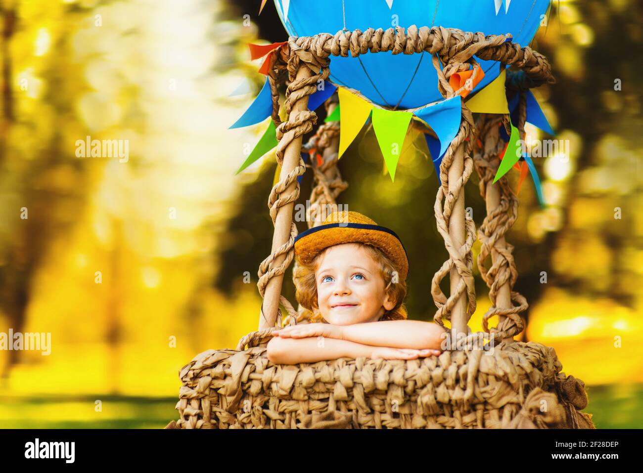 Little curly-haired boy in the air dreaming looks into the sky. Baby in a balloon basket. Stock Photo