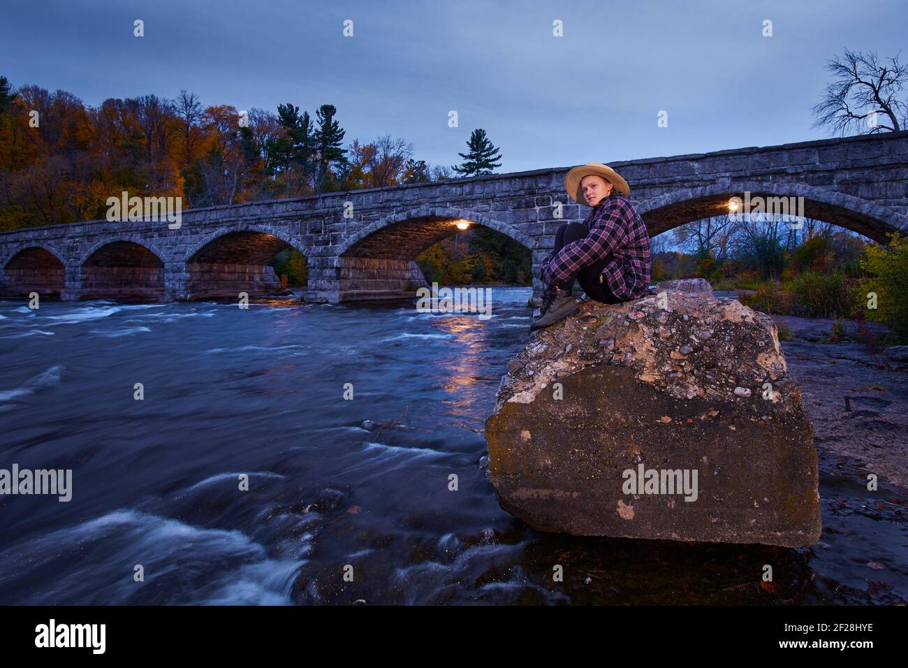 Young woman sitting on the rocks, downstream of the Pakenham Bridge in