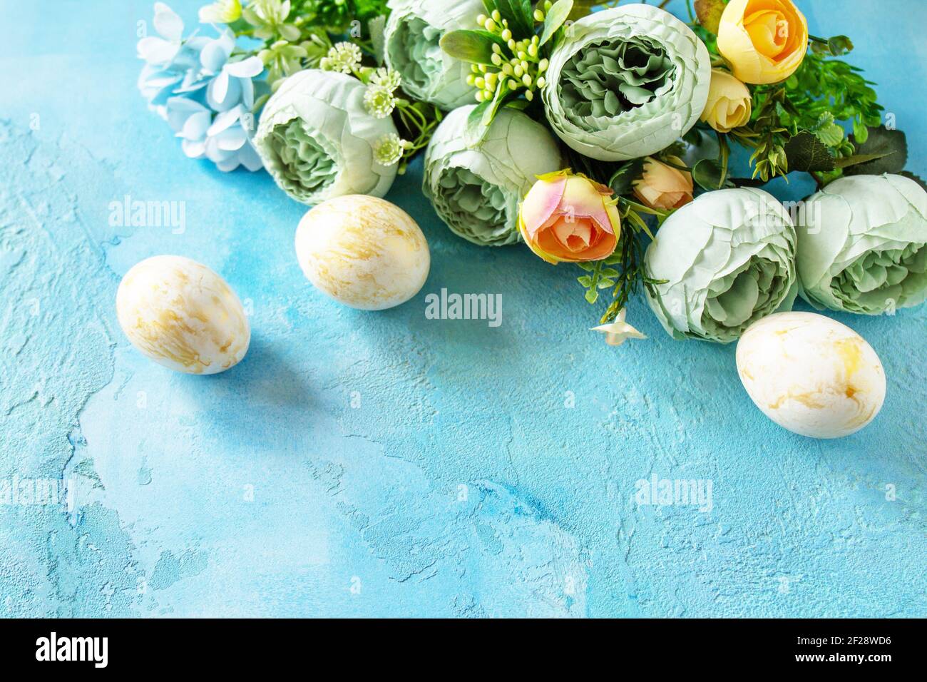 Happy Easter background. Spring flowers and Easter eggs on a concrete blue background. Stock Photo
