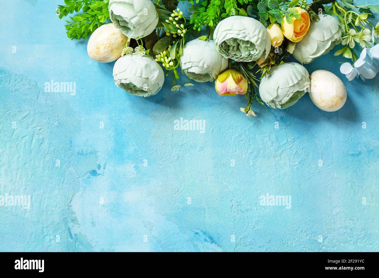 Happy Easter background. Spring flowers and Easter eggs on a concrete blue background. Top view flat lay. Stock Photo