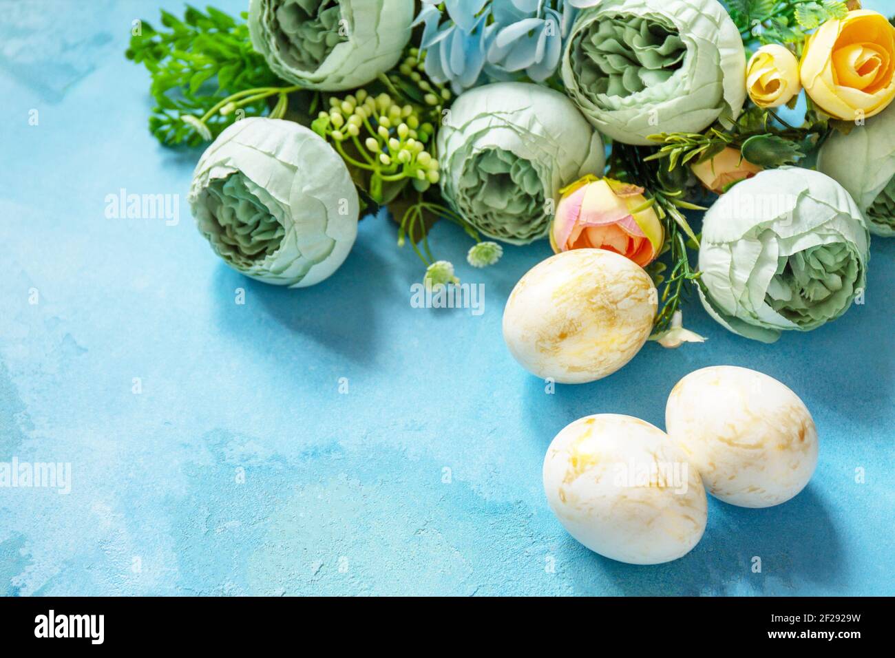 Happy Easter background. Spring flowers and Easter eggs on a concrete blue background. Stock Photo