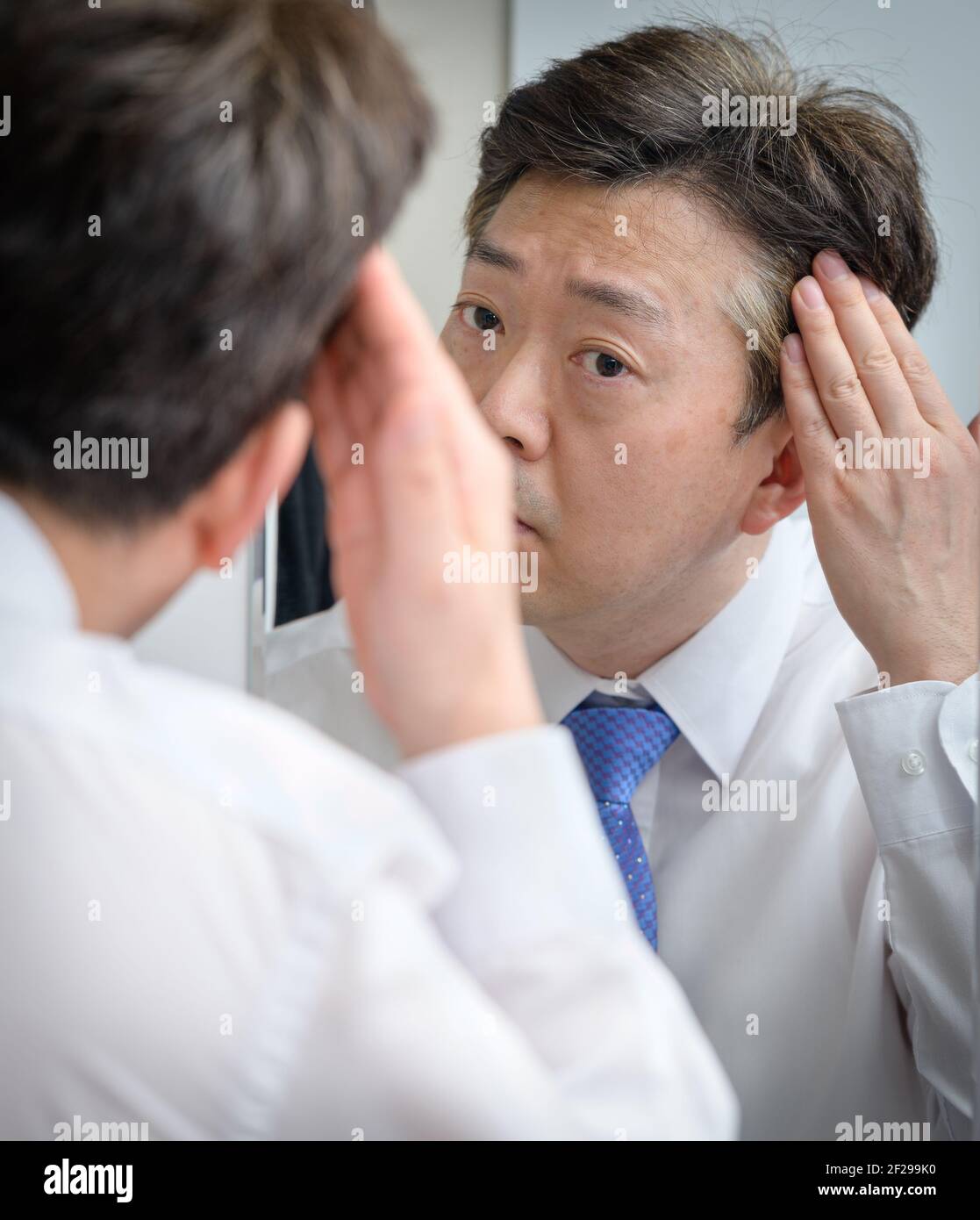 Asian middle-aged man looking in the mirror and touching his hair Stock Photo